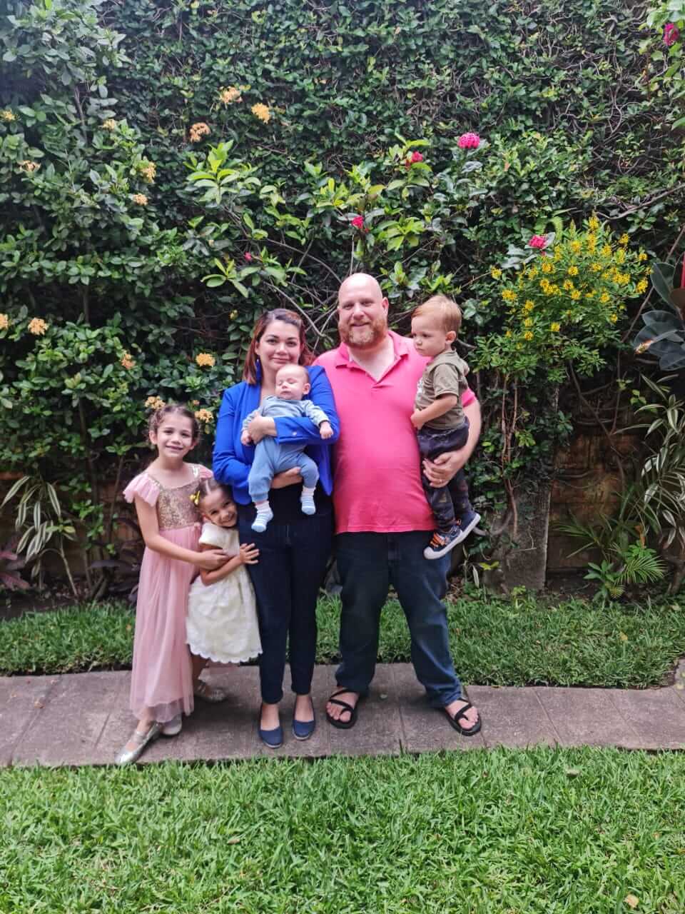 A photo of the Jedlika family standing outside in front a tropical plant background